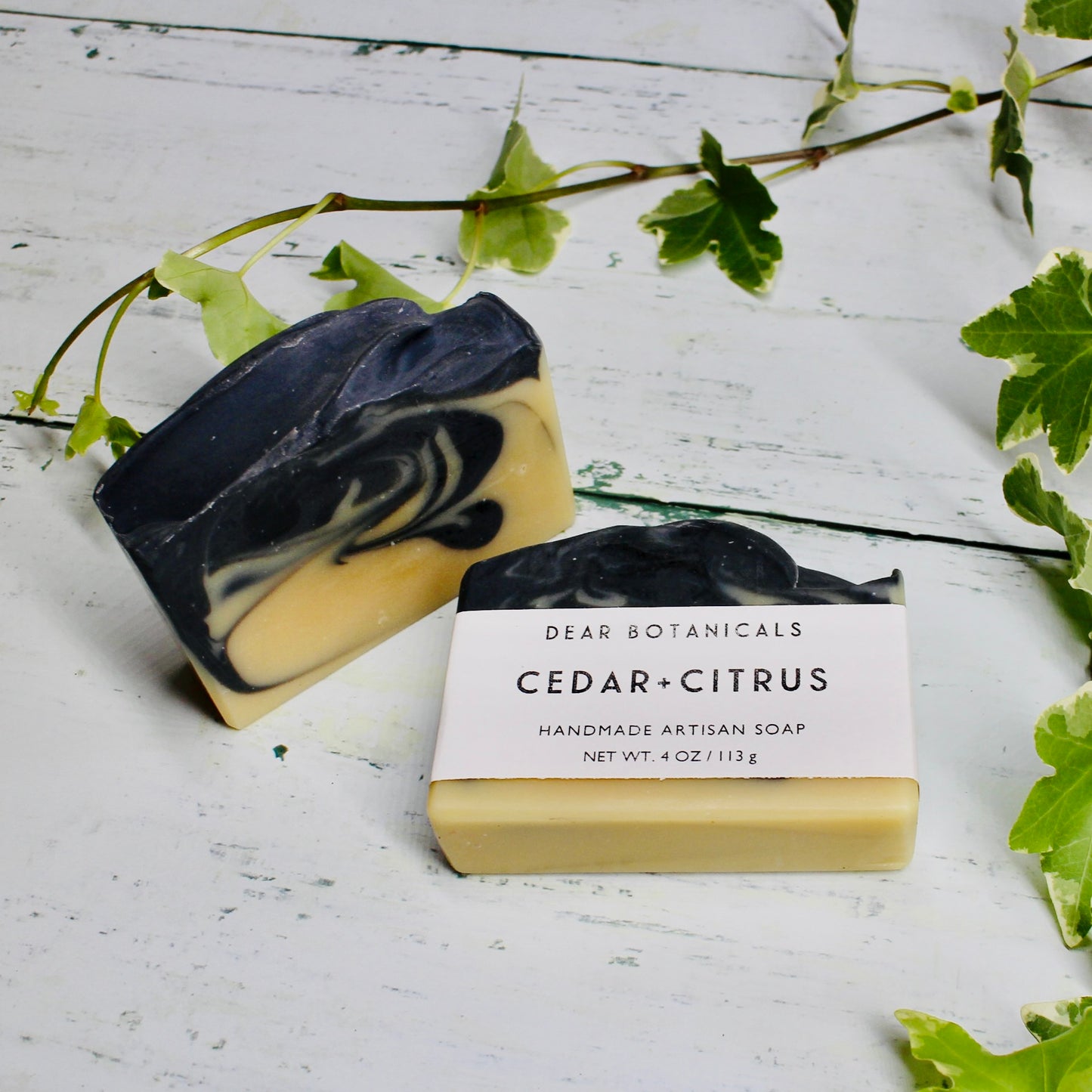Dear Botanicals Cedar and Citrus Soap. Dark blue and yellow swirl colour, white card and black text branding wrapped around soap.